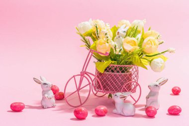 Gentle Easter greeting card with spring flowers, rabbit, eggs and traditional decor. Happy holiday concept, hard light, dark shadow, pink background, copy space
