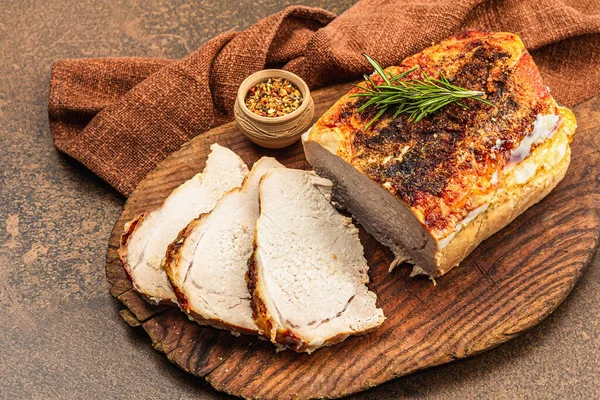 Baked pork loin with spices and herbs on vintage wooden cutting board. Ready to eat meat slices, healthy lifestyle, dinner concept. Brown stone background, flat lay, close up