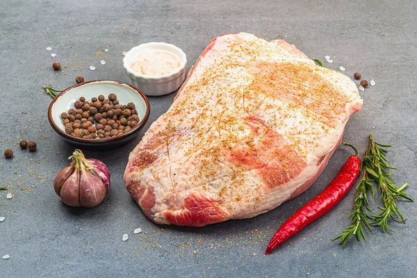 Raw pork shoulder with spices and herbs. Fresh meat cut, ingredient for cooking protein food, healthy food lifestyle. Grey stone concrete background, close up