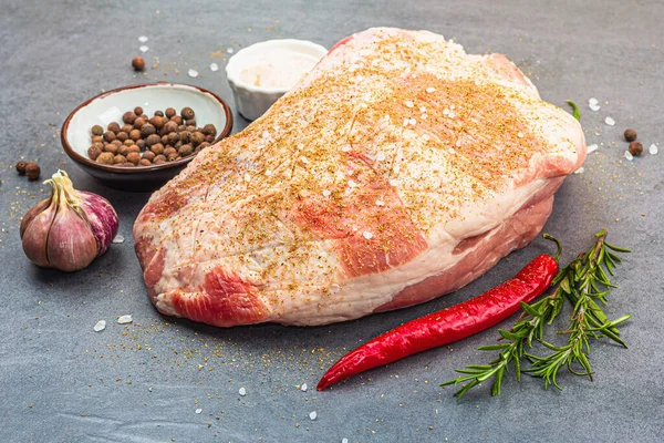 Raw pork shoulder with spices and herbs. Fresh meat cut, ingredient for cooking protein food, healthy food lifestyle. Grey stone concrete background, close up