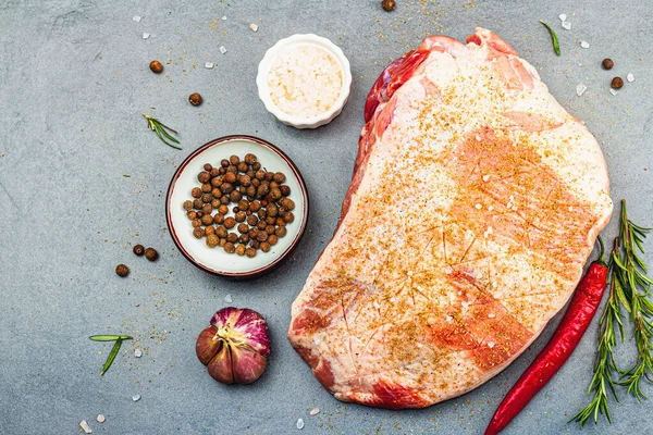 Raw pork shoulder with spices and herbs. Fresh meat cut, ingredient for cooking protein food, healthy food lifestyle. Grey stone concrete background, top view
