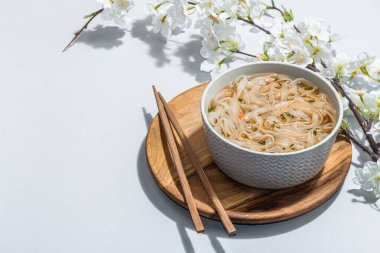 Kore eriştesi çorbalı Ramen. Sıcak yemek, yemek çubukları, sert ışık, karanlık gölge. Gri arkaplan, kiraz çiçekleri, düz yatak, kopyalama alanı