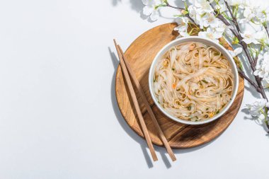 Kore eriştesi çorbalı Ramen. Sıcak yemek, yemek çubukları, sert ışık, karanlık gölge. Gri arkaplan, kiraz çiçekleri, düz yatak, üst manzara