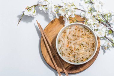Kore eriştesi çorbalı Ramen. Sıcak yemek, yemek çubukları, sert ışık, karanlık gölge. Gri arkaplan, kiraz çiçekleri, düz yatak, üst manzara