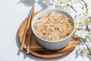 Kore eriştesi çorbalı Ramen. Sıcak yemek, yemek çubukları, sert ışık, karanlık gölge. Gri arkaplan, kiraz çiçekleri, düz yatak, kopyalama alanı
