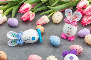 Paskalya düzlüklerinde sevimli tavşanlar, yumurtalar ve laleler vardı. Geleneksel dekor, bayram tebrik kartı, tatil konsepti, gri taş beton arka plan, kapat