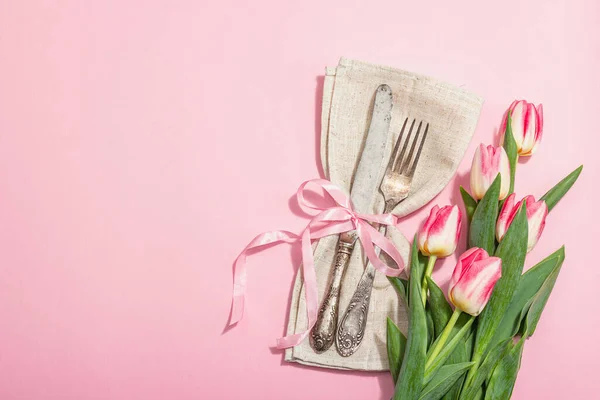 stock image Romantic table setting with pink tulips. Vintage cutlery, fresh flowers, linen napkin. Festive concept background, flat lay, hard light, dark shadow, top view