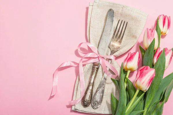 stock image Romantic table setting with pink tulips. Vintage cutlery, fresh flowers, linen napkin. Festive concept background, flat lay, hard light, dark shadow, top view