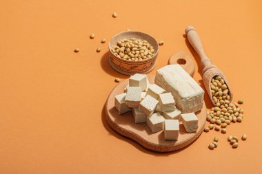 Soya fasulyeli taze tofu peyniri. Küp parçaları, vejetaryen yaşam tarzı için sağlıklı malzeme, modern duruş, modaya uygun sert ışık, karanlık gölge. Parlak turuncu arkaplan, düz yatış, kopyalama alanı