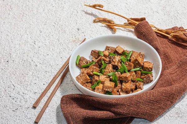 Kızarmış teriyaki tofu, soğanlı ve susamlı. Protein ve kalsiyum açısından zengin sağlıklı vejetaryen eti. Moda sabit ışık, koyu gölge, alçı arkaplan, kopyalama alanı