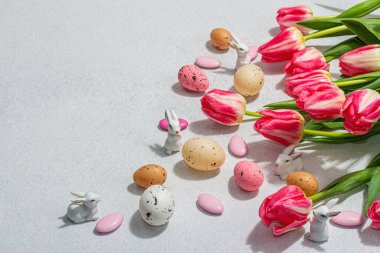 Paskalya yumurtalı pembe laleler ve parlak beton arka planda tavşanlar. Kutlama konsepti, tebrik kartı, düz konum, sert ışık, karanlık gölge, kopyalama alanı