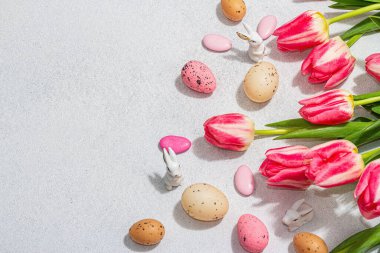 Paskalya yumurtalı pembe laleler ve parlak beton arka planda tavşanlar. Kutlama konsepti, tebrik kartı, düz konum, sert ışık, koyu gölge, üst görünüm