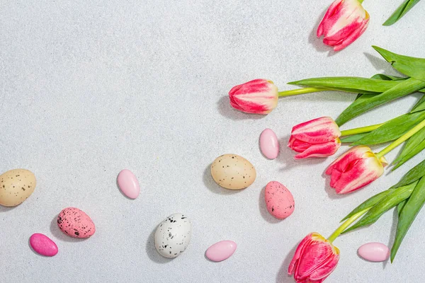 stock image Pink tulips with Easter eggs on light stone concrete background. Festive concept, greeting card, flat lay, hard light, dark shadow, top view