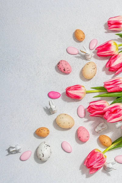 stock image Pink tulips with Easter eggs and rabbits on light stone concrete background. Festive concept, greeting card, flat lay, hard light, dark shadow, top view