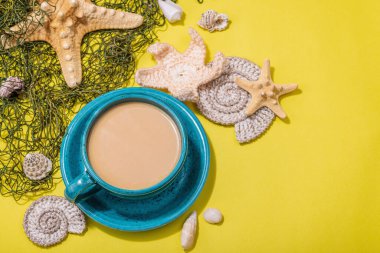 Deniz usulü bir fincan kahve. Deniz yıldızı, deniz kabukları, palmiye yaprakları. Sert ışık, koyu gölge, parlak sarı arkaplan, boşluğu kopyala