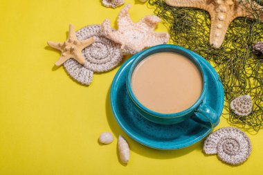 Deniz usulü bir fincan kahve. Deniz yıldızı, deniz kabukları, palmiye yaprakları. Sert ışık, koyu gölge, parlak sarı arkaplan, boşluğu kopyala