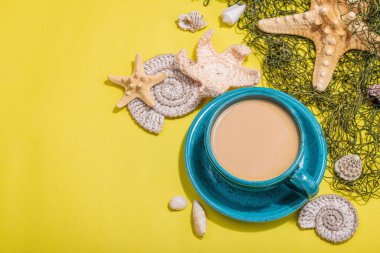 Deniz usulü bir fincan kahve. Deniz yıldızı, deniz kabukları, palmiye yaprakları. Sert ışık, koyu gölge, parlak sarı arkaplan, boşluğu kopyala