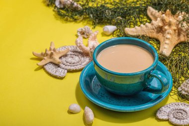 Deniz usulü bir fincan kahve. Deniz yıldızı, deniz kabukları, palmiye yaprakları. Sert ışık, koyu gölge, parlak sarı arkaplan, boşluğu kopyala