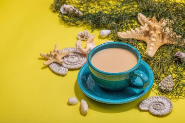 Deniz usulü bir fincan kahve. Deniz yıldızı, deniz kabukları, palmiye yaprakları. Sert ışık, koyu gölge, parlak sarı arkaplan, boşluğu kopyala