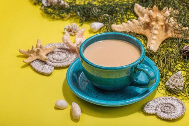 Deniz usulü bir fincan kahve. Deniz yıldızı, deniz kabukları, palmiye yaprakları. Sert ışık, koyu gölge, parlak sarı arkaplan, kapat