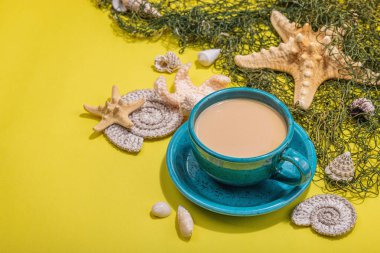 Deniz usulü bir fincan kahve. Deniz yıldızı, deniz kabukları, palmiye yaprakları. Sert ışık, koyu gölge, parlak sarı arkaplan, boşluğu kopyala