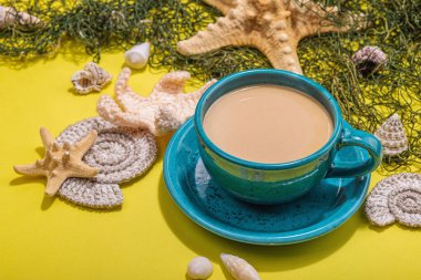 Deniz usulü bir fincan kahve. Deniz yıldızı, deniz kabukları, palmiye yaprakları. Sert ışık, koyu gölge, parlak sarı arkaplan, kapat