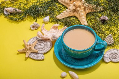 Deniz usulü bir fincan kahve. Deniz yıldızı, deniz kabukları, palmiye yaprakları. Sert ışık, koyu gölge, parlak sarı arkaplan, kapat