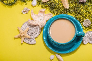 Deniz usulü bir fincan kahve. Deniz yıldızı, deniz kabukları, palmiye yaprakları. Sert ışık, koyu gölge, parlak sarı arkaplan, boşluğu kopyala