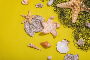 Deniz kabukları, deniz yıldızları ve balık ağlarıyla donatılmış sarı bir arka plan. Çeşitli deniz hayvanları, tatil konsepti. Modaya uygun sert ışık, koyu gölge, düz uzanma, üst manzara