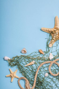 Deniz kabukları, deniz yıldızları ve balıkçı ağıyla donatılmış mavi bir arka plan. Çeşitli deniz hayvanları, tatil konsepti. Modaya uygun sert ışık, koyu gölge, düz uzanma, üst manzara
