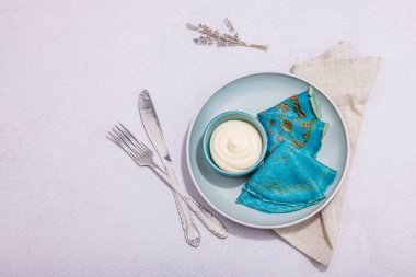 Krema soslu ince mavi krep. Sağlıklı vegan, laktoz ve glütensiz yemek, kahvaltı konsepti. Modaya uygun sert ışık, karanlık gölge, aydınlık taş arkaplan, üst görünüm