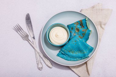 Krema soslu ince mavi krep. Sağlıklı vegan, laktoz ve glütensiz yemek, kahvaltı konsepti. Modaya uygun sert ışık, karanlık gölge, aydınlık taş arkaplan, üst görünüm
