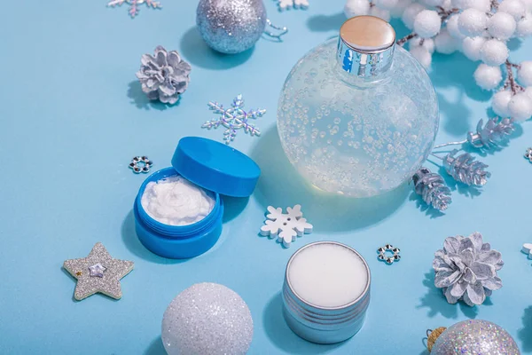 Winter season skin care cosmetics concept. Set with moisturizing lotion, nourishing cream and shea butter.Traditional Christmas decor, New Year props. Blue background, close up