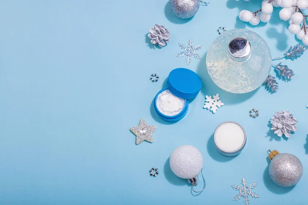 Winter season skin care cosmetics concept. Set with moisturizing lotion, nourishing cream and shea butter.Traditional Christmas decor, New Year props. Blue background, top view