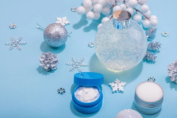 Winter season skin care cosmetics concept. Set with moisturizing lotion, nourishing cream and shea butter.Traditional Christmas decor, New Year props. Blue background, close up