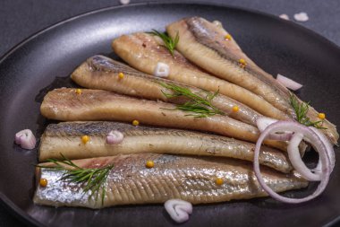 Soğan ve dereotlu salamura deniz ringa balığı filetosu. Deniz ürünleri, sert ışık ve karanlık gölge yemeye hazır. Siyah taş zemin, düz zemin, yakın plan.