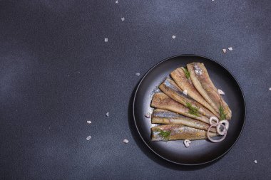 Soğan ve dereotlu salamura deniz ringa balığı filetosu. Deniz ürünleri, sert ışık ve karanlık gölge yemeye hazır. Siyah taş zemin, düz zemin, üst manzara