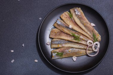 Soğan ve dereotlu salamura deniz ringa balığı filetosu. Deniz ürünleri, sert ışık ve karanlık gölge yemeye hazır. Siyah taş zemin, düz zemin, üst manzara