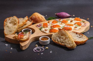 Somon, arpacık soğanı ve taze yeşilliklerle süslenmiş tereyağlı yiyecek trendi. Parti için aperatif, baget parçaları, sert ışık, karanlık gölge. Siyah taş zemin, düz zemin, kopyalama alanı