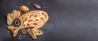 Somon, arpacık soğanı ve taze yeşilliklerle süslenmiş tereyağlı yiyecek trendi. Parti için aperatif, baget parçaları, sert ışık, karanlık gölge. Siyah taş zemin, düz zemin, pankart biçimi