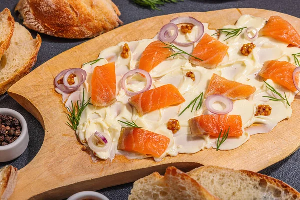 stock image Butter Board food trend topped with salmon, shallots and fresh greens. Appetizer for a party, baguette pieces, hard light, dark shadow. Black stone concrete background, flat lay, close up