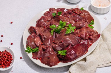 Taş zeminde çiğ tavuk ciğeri. Yemek, maydanoz ve kırmızı biber için taze malzemeler hazır. Modaya uygun sert ışık, karanlık gölge, düz uzanma, yakın çekim