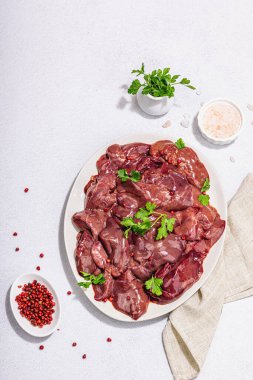 Taş zeminde çiğ tavuk ciğeri. Yemek, maydanoz ve kırmızı biber için taze malzemeler hazır. Modaya uygun sert ışık, koyu gölge, düz uzanma, üst manzara