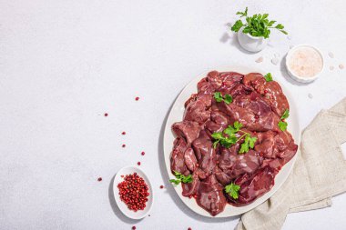 Taş zeminde çiğ tavuk ciğeri. Yemek, maydanoz ve kırmızı biber için taze malzemeler hazır. Modaya uygun sert ışık, koyu gölge, düz uzanma, üst manzara