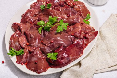 Taş zeminde çiğ tavuk ciğeri. Yemek, maydanoz ve kırmızı biber için taze malzemeler hazır. Modaya uygun sert ışık, karanlık gölge, düz uzanma, yakın çekim