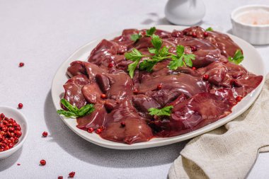 Taş zeminde çiğ tavuk ciğeri. Yemek, maydanoz ve kırmızı biber için taze malzemeler hazır. Modaya uygun sert ışık, karanlık gölge, düz uzanma, yakın çekim