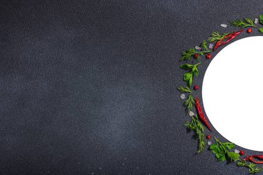 Taze maydanoz ve dereotlu çelenk, acı biber, koyu beton zeminde deniz tuzu. Yuvarlak çerçeve, modern sert ışık, koyu gölge, düz yer, üst manzara