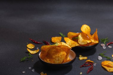 Kırmızı biber, maydanoz ve siyah beton arka planda tuz ile servis edilen ev yapımı patates cipsi kaseleri. Moda sabit ışık, karanlık gölge, boşluğu kopyala