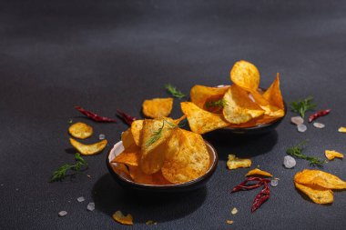 Kırmızı biber, maydanoz ve siyah beton arka planda tuz ile servis edilen ev yapımı patates cipsi kaseleri. Moda sabit ışık, karanlık gölge, boşluğu kopyala