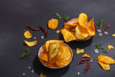 Kırmızı biber, maydanoz ve siyah beton arka planda tuz ile servis edilen ev yapımı patates cipsi kaseleri. Moda sabit ışık, karanlık gölge, boşluğu kopyala
